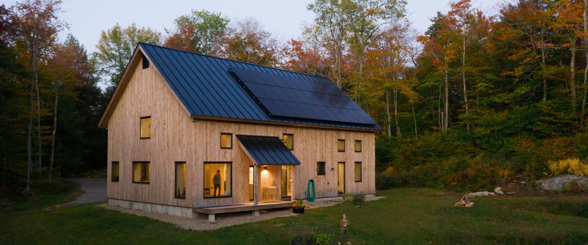 A gable-roofed home in the forest with natural siding and a roof full of solar power.