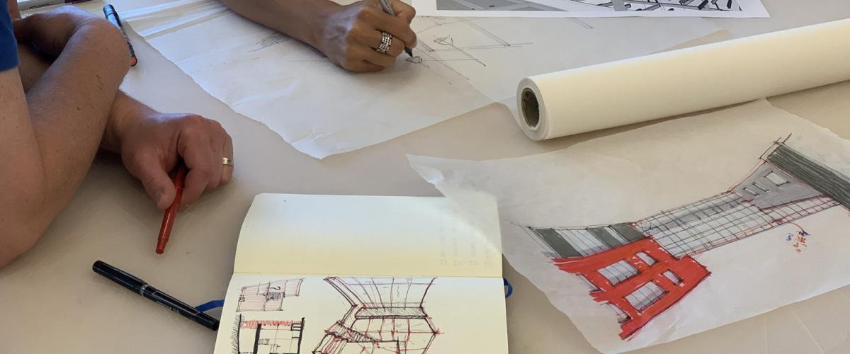 Tabletop with people sketching buildings in book and on tracing paper