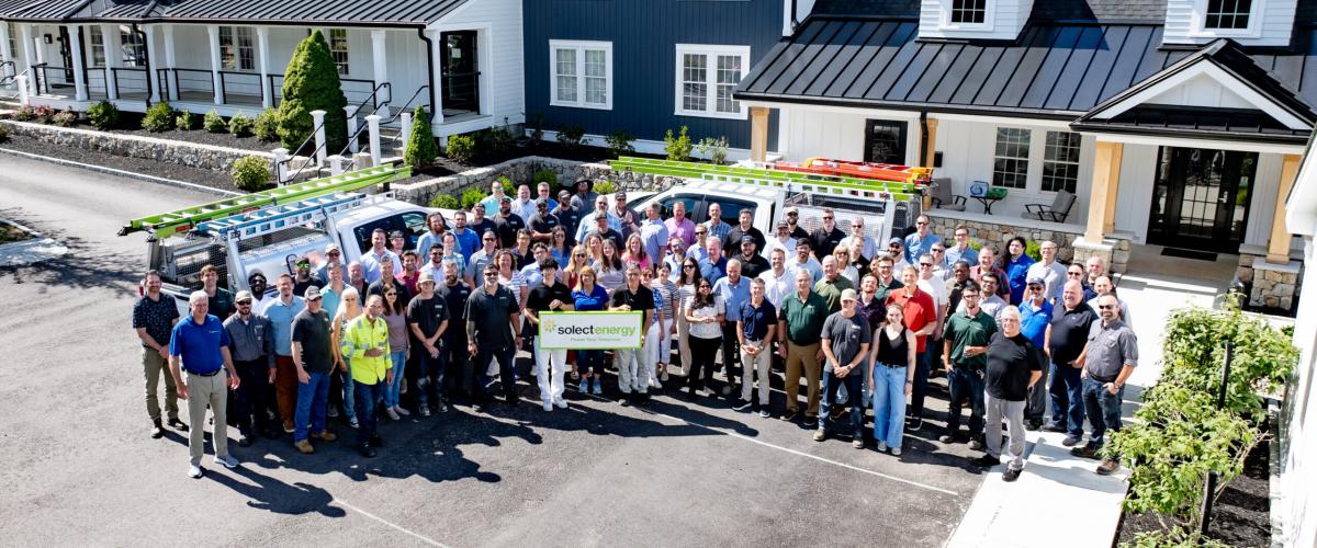 A large group of people posing together in a parking lot, with two people in the center holding a "Solect Energy" sign.