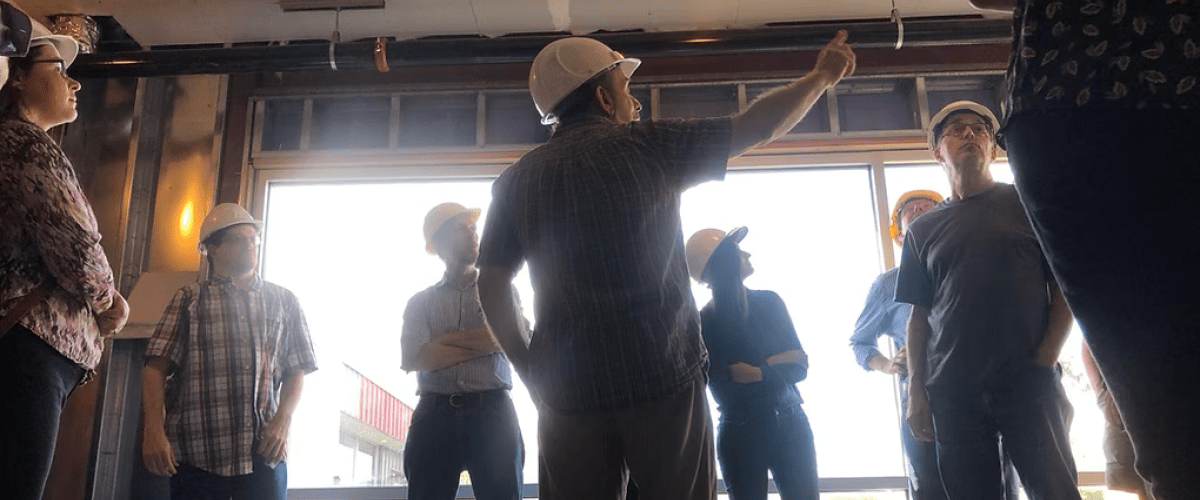 Taitem staff, wearing white hard hats, viewing the interior of a raw building space.