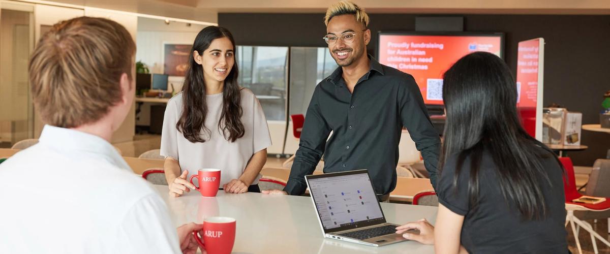 Four professionals gathered around a table within an Arup office with Arup branded coffee cups in hand