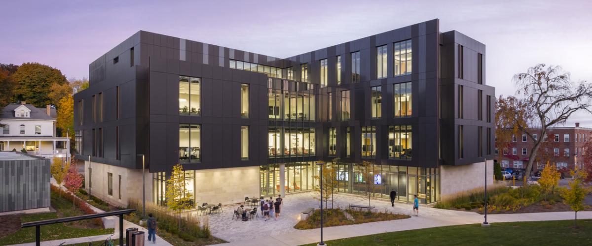 Exterior view of the academic building overlooking a landscaped courtyard, with transparent façades revealing interior makerspaces and collaborative learning areas as students move through the campus.