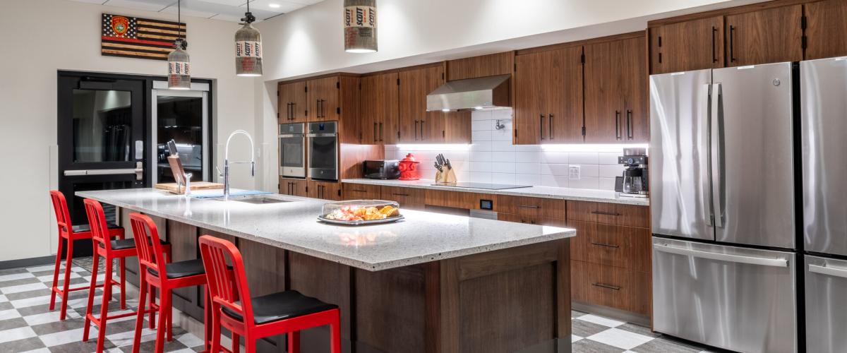 Kitchen shot showing checker tiled floor, all electric appliances, and bright red stools at a big floating island.