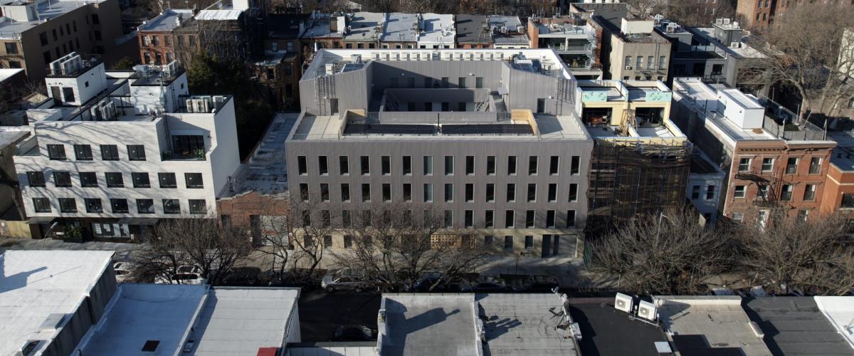 A modern, four-story gray residential building with a flat roof and a central courtyard.