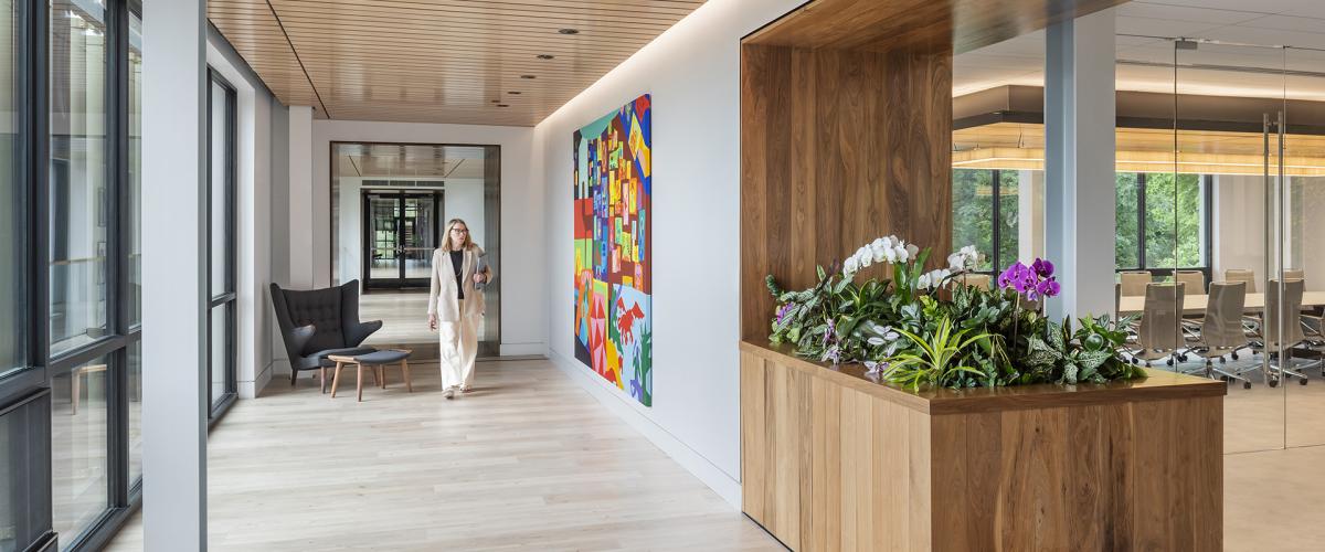A modern, well-lit hallway with a wood ceiling, featuring a large colorful painting on the wall and a built-in wooden planter with orchids in the foreground.