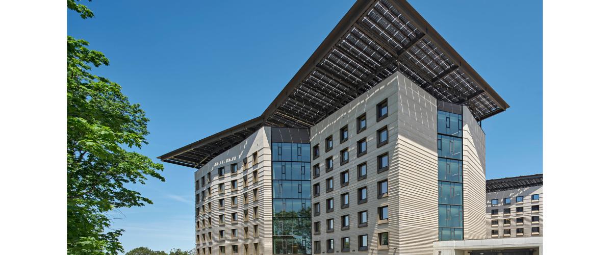 Exterior daytime photo looking up at the six floor building with large rooftop solar array canopy stretching over like an umbrella