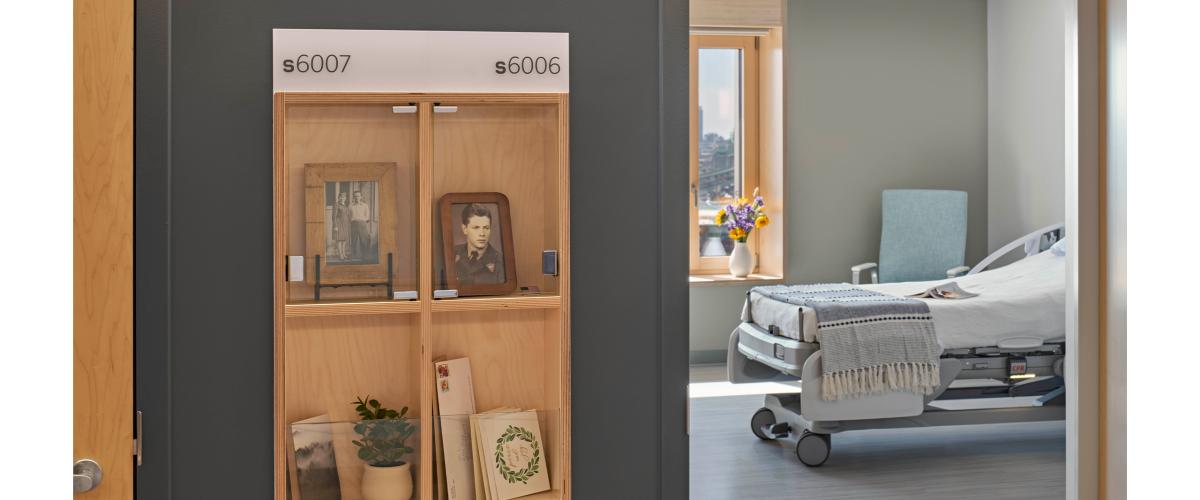 A small shelf of important personal mementos is seen outside the doorway of a residents room. A healthcare style bed is seen through the opening.