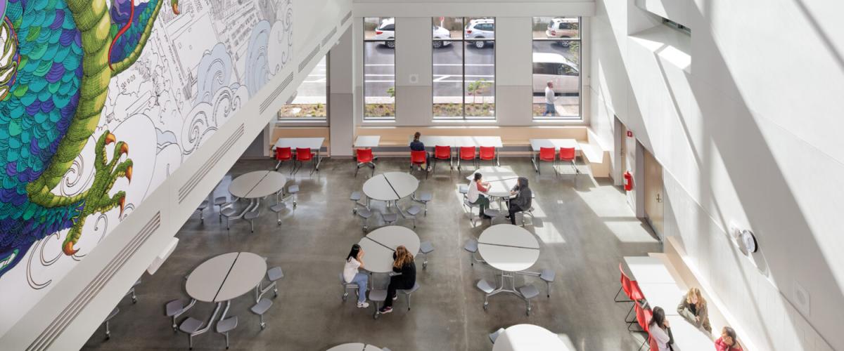 A three story open space above the cafeteria features a mural with a red phoenix and a blue green dragon over a aerial sketch of the school's neighborhood