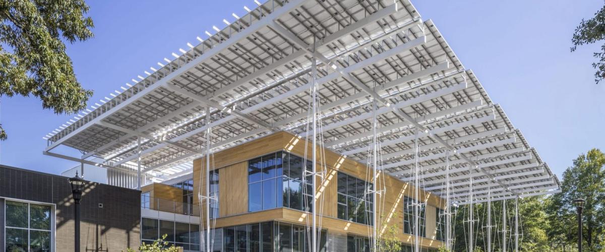 A modern building exterior with a large, prominent solar panel canopy extending over the entrance and surrounding walkways.