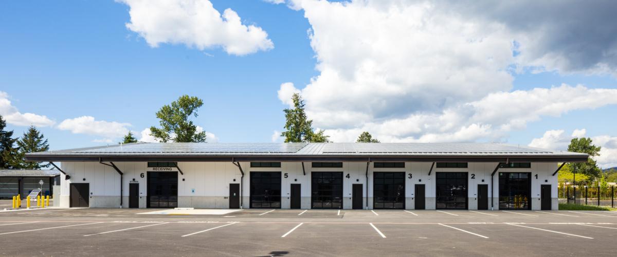 A modern industrial building featuring a row of dark garage doors and a solar array on the roof.