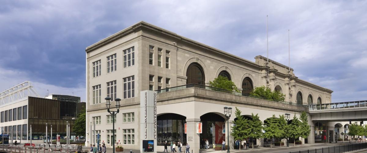 A daytime view of the revitalized Commonwealth Pier, featuring its blend of historic maritime architecture and modern public spaces along a paved waterfront road.