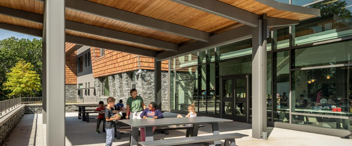 Exterior view showing a covered outside classroom space featuring picnic tables and a wood ceiling.