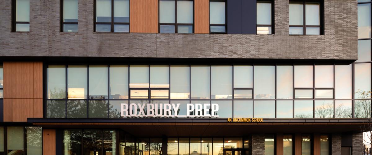 Street‑level view of the Roxbury Prep entrance, showing large windows and students walking along the front sidewalk.