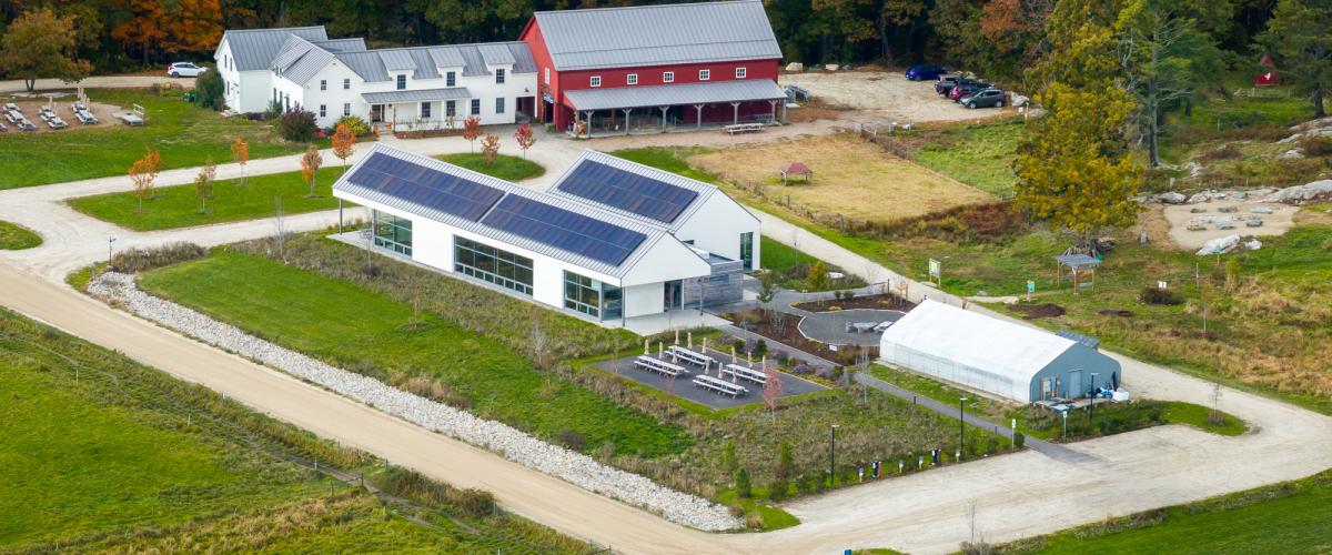 Aerial view of the center, featuring a modern building with solar panels alongside a traditional red barn and white farmhouse.