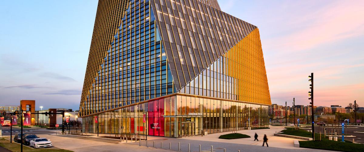 A low-angle view of a modern, geometric building, featuring a glass facade with gold-colored accents against a twilight sky.