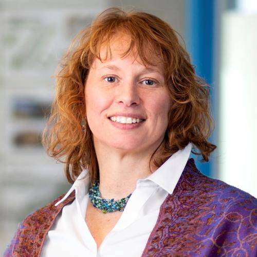 Head shot of woman with wavy red hair wearing a button-down shirt and shawl