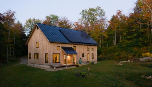 A gable-roofed home in the forest with natural siding and a roof full of solar power.