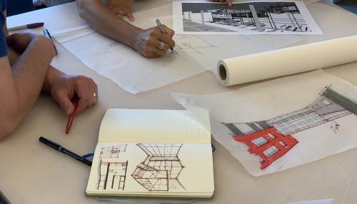 Tabletop with people sketching buildings in book and on tracing paper