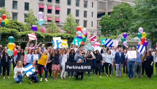 Employees gathered in a park with balloons and the Perkins&Will logo on a sign