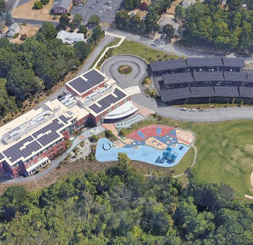 Aerial view of Maria Hastings Elementary School showing rooftop solar arrays and solar canopies above parking area