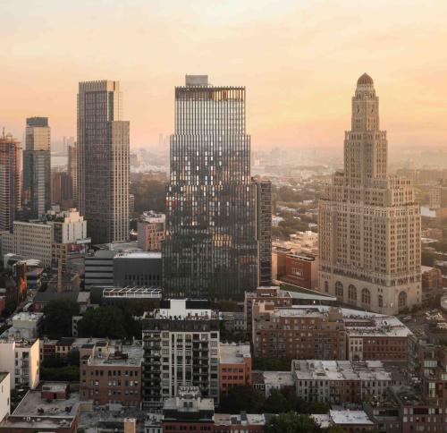 A golden-hour view of the Brooklyn skyline featuring a modern stepped glass skyscraper at its center.