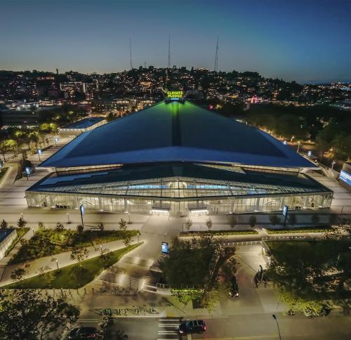 An aerial view of Climate Pledge Arena at dusk, featuring its distinctive, sweeping roofline and illuminated exterior.
