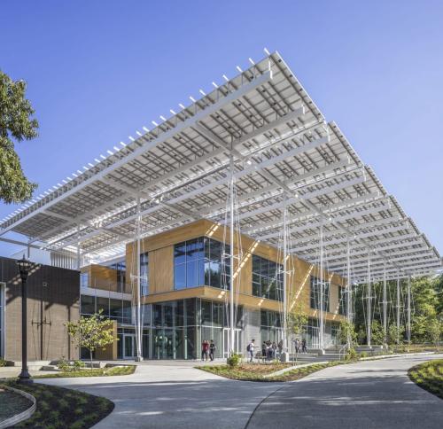 A modern building exterior with a large, prominent solar panel canopy extending over the entrance and surrounding walkways.