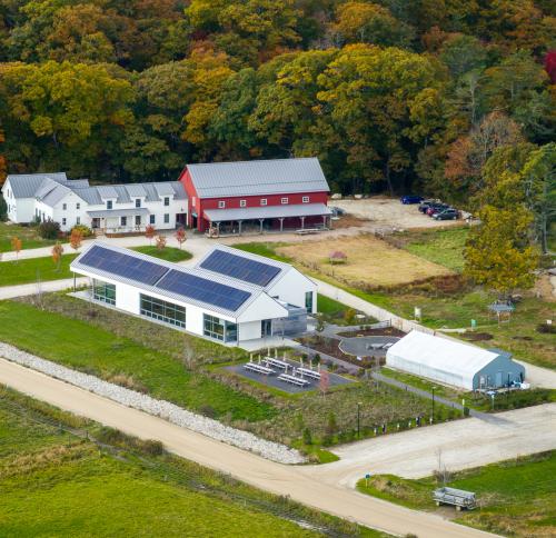 Aerial view of the center, featuring a modern building with solar panels alongside a traditional red barn and white farmhouse.